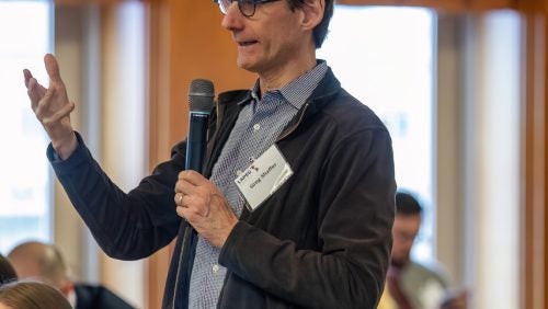 Greg Shaffer is asking a question his feet while holding a microphone.