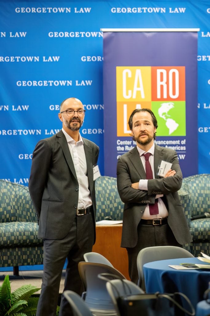 Professors Alvaro Santos and Nicolas Perrone seen standing in front of the main podium with the CAROLA banner behind them.
