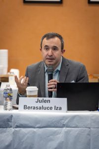 Professor Julen Berasaluce holding a microphone while speaking seated at a table