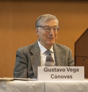 Professor Gustavo Vega smiling seating at a table with a name tent showing his name