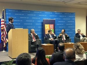 Professor Alvaro Santos is speaking holding a microphone while the other members of the panel listen