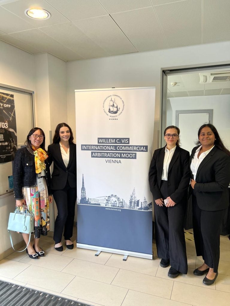 2025 Vis Moot team standing with a Vis Moot banner