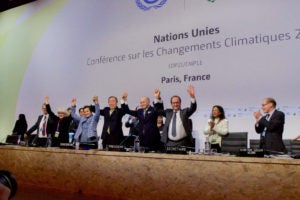 Several world leaders meet at the UN in Paris. Some have their hands linked and raised above their heads. Two others are clapping. 