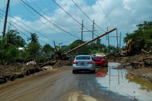 A line of cars navigating a partially flooded dirt road with fallen trees and damaged power lines. (Reuters.com, September 26, 2022, About 746,000 still without power in Puerto Rico after Hurricane Fiona).