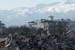 Rubble from collapsed and heavily damaged buildings in the foreground with snowcapped mountains visible in the background.