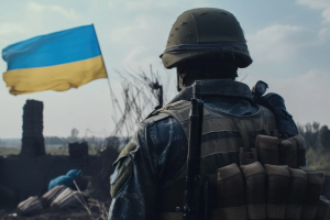 A soldier looks towards a Ukrainian flag flying on a battlefield