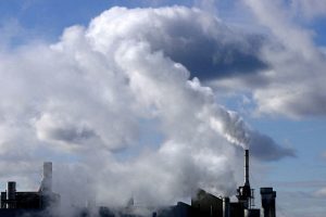 Heavy industrial pollution leaving smokestacks in blue sky. 