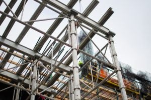 Tower construction site seen through scaffolding with workers suspended in the background