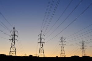 Several transmission towers carry large power lines at dusk.