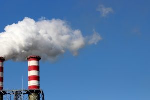 Two smokestacks releasing clouds of pollutants into the air. Major sources of ground-level ozone pollution include emissions from industrial activity, electricity generation, and vehicle exhaust.