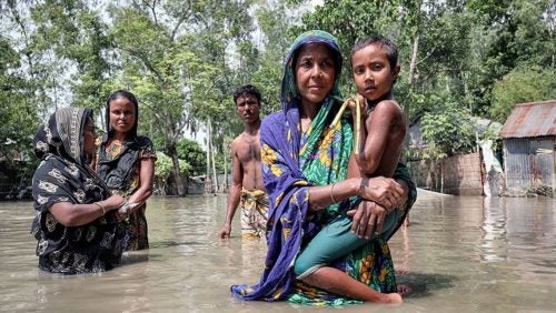 People wading through floodwaters illustrate human vulnerability to climate impacts.