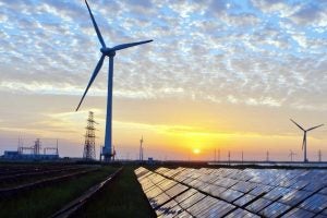 Solar cell panels, wind turbines, and electricity pylons at sunset.