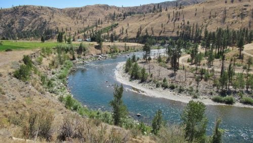 A blue river runs across scrub land next to a hill.