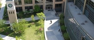 Photo of Georgetown Law's Campus, depicting the Clock Tower and Hotung Building with a person walking towards the building entrance.