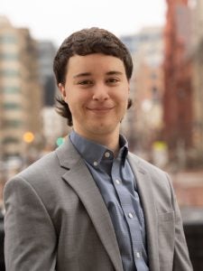 Man with brown hair in grey blazer and blue shirt.