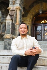 Man in white shirt and black pants on steps of stone building.