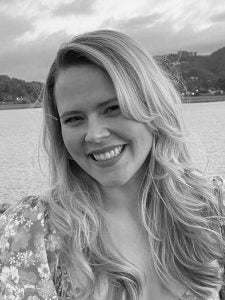 Black and white picture of woman in front of lake and mountains.