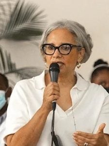 Madame Mildred Trouillot-Aristide speaking in group wearing white shirt and black glasses