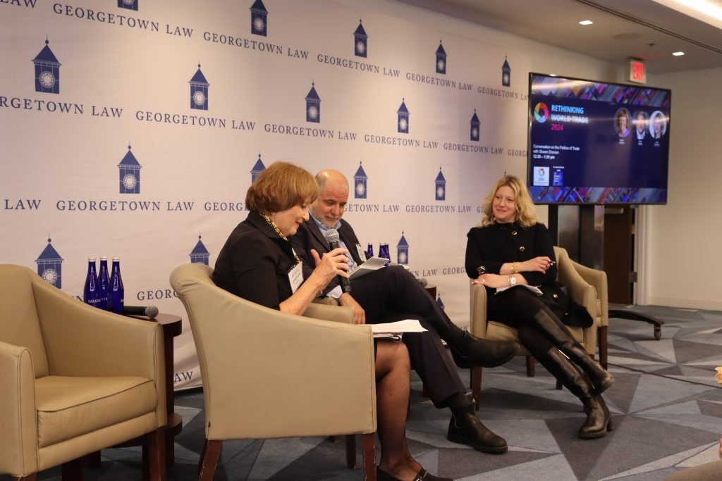 From left to right, Jennifer Hillman, Shawn Donnan, and Katrin Kulhmann sit in chairs in front of a Georgetown Law backdrop with microphones.