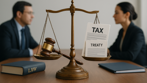 An image of the scales of justice on a table, with a court gavel on the left scale and documents titled "Tax" and "Treaty" on the right scale. In the background of the image, there are two business people that are slightly blurred.