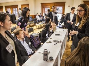 Students dressed in business clothing mingle around a long table