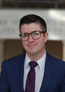 Headshot of James Carey, a young man in a suit and glasses.