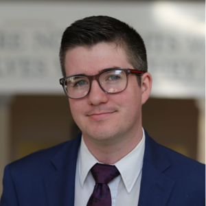 Headshot of James Carey, a man with glasses and a blue suit.