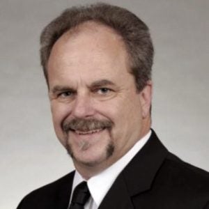 Headshot of Ron Prevost, a man smiling in a suit with a beard.