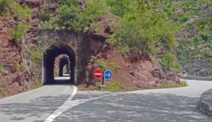 A mountain road with a splitting path, one side with an arrow and the other a "wrong way" sign