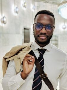 A man with glasses and wearing a tie with his jacket slung over his shoulder.