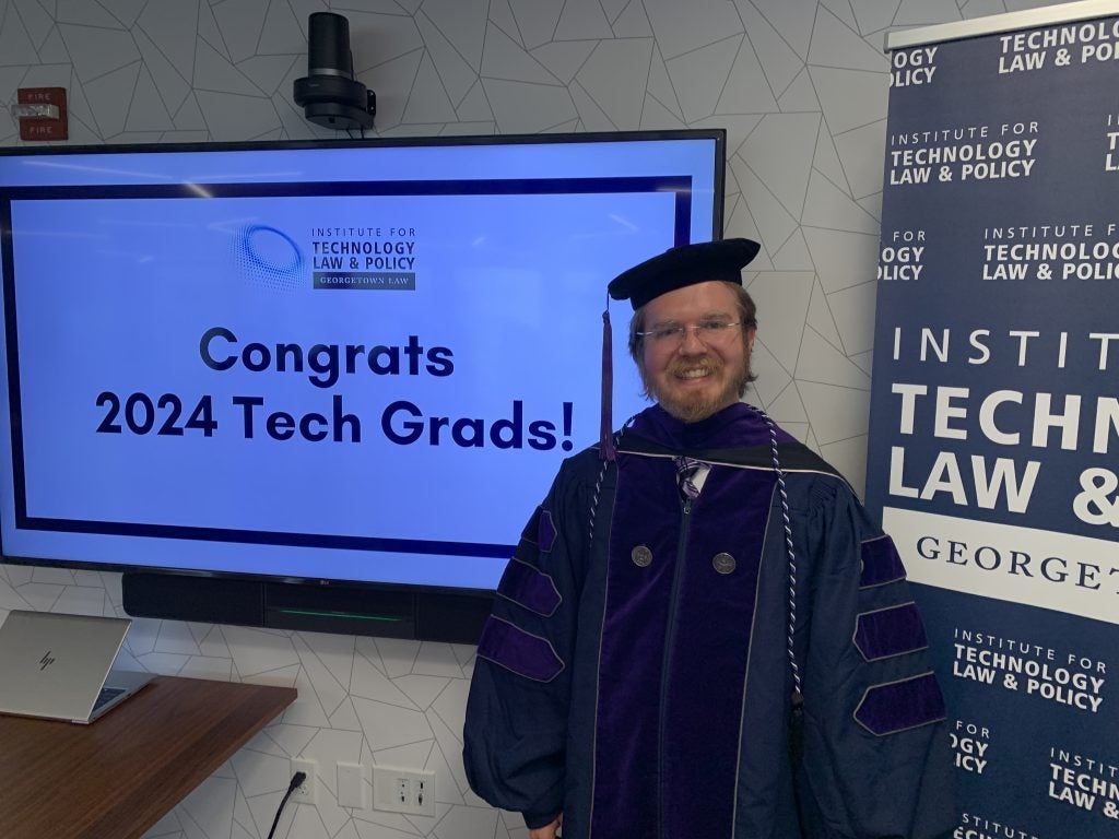 Logan Arkema in front of a sign that reads "Congrats 2024 Tech Grads!"