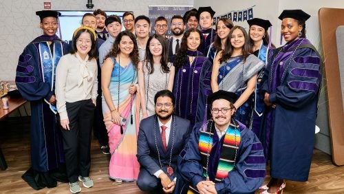 Twenty people, many of them wearing academic regalia, pose together.