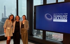 3 Tech Institute staff members stand smiling next to a Tech Institute Sign at Cooley LLP's Office.