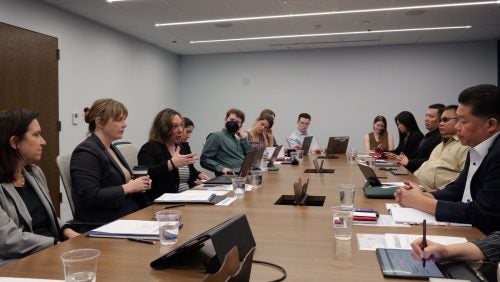 Many people in discussion around a table, with paper notes and computers open.