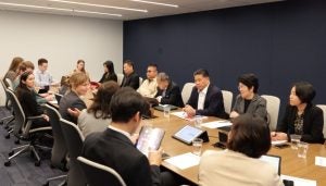 Many people in discussion around a table, including the Thai Delegation, with paper notes and computers open.