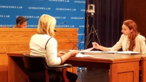 Two students seated at a table conducting negotiations in front of a judge at a judges bench.