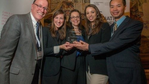 Five people standing together, smiling, holding a glass plaque.