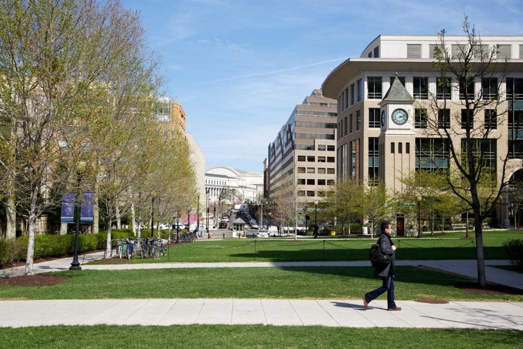 student walking on Law Center campus with Clock Tower and Hotung building on the right hand side.