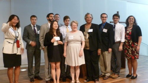 Clinical students and director standing on stage smiling at the UCC breakfast. 