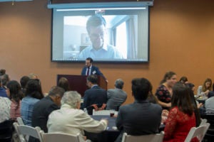 Georgetown Law Professor Alvaro Santos, at podium, introduces Columbia Law Professor Jeffrey Sachs, onscreen, via video from Madrid.