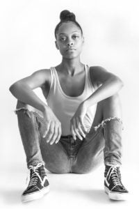 Photograph of African American girl wearing jeans and a t-shirt, sitting on the floor.