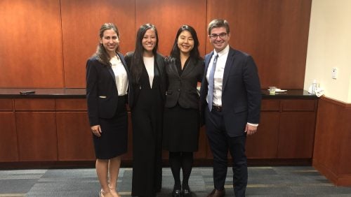 Four students standing together, smiling, in suits