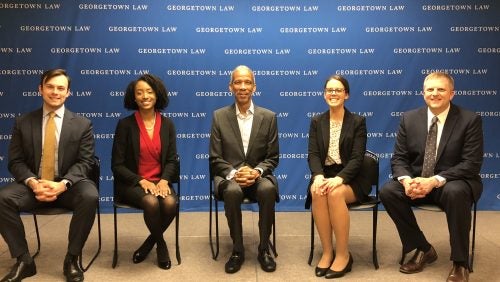 Five people seated in front of blue background with the words GEORGETOWN LAW on it.