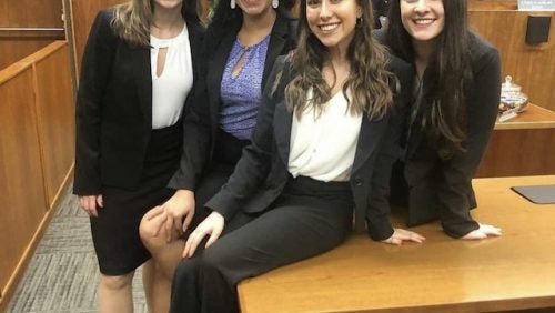 Four women in suits sitting on a table smiling