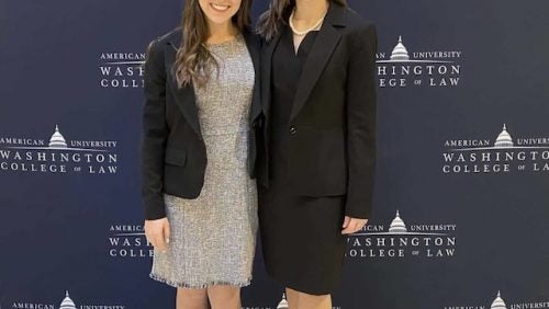 Two women smiling in front of American University Washington College of Law Banner