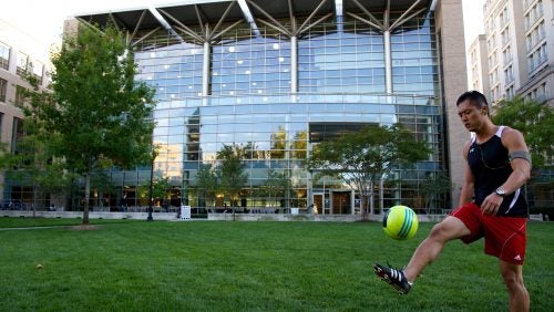 student kicking soccer ball in front of the Scott K. Ginsburg Sport & Fitness Center