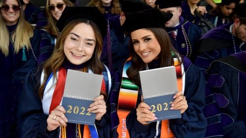 Two students smiling and holding up the commencement ceremony program booklet