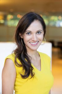 Anjali Patel, a woman with long dark hair wearing yellow