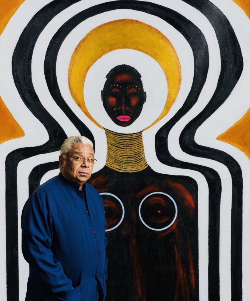 Artist LeRoi Johnson standing next to a large painting of a Black woman with gold ornaments on her neck and black and gold lines outlining her form.