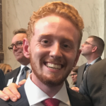 A young man with red hair and beard, smiling